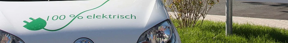 Ausschnitt Motorhaube eines Elektrofahrzeugs mit der Aufschrift 100% elektrich und einem grünen Stromkabel.