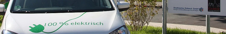 Ausschnitt Motorhaube eines Elektrofahrzeugs mit der Aufschrift 100% elektrich und einem grünen Stromkabel.